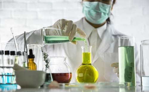In a beauty industry setting, a scientist samples a chemical extract from organic materials.