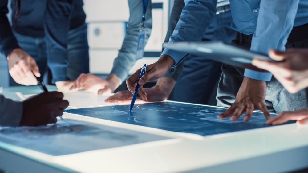 A close-up view of an illuminated conference table in a collaborative workspace, with blueprints spread out, indicating creative engineering work in progress.