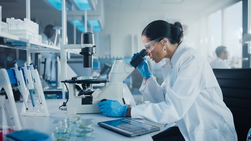 A female scientist in a medical development laboratory, looking under a microscope while analyzing samples.
