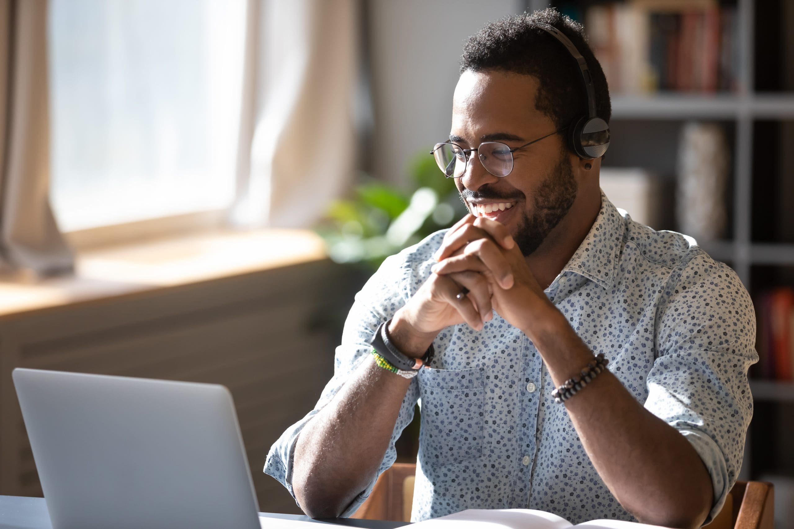 A man in a white shirt smiles while working on a laptop, possibly applying for a grant.