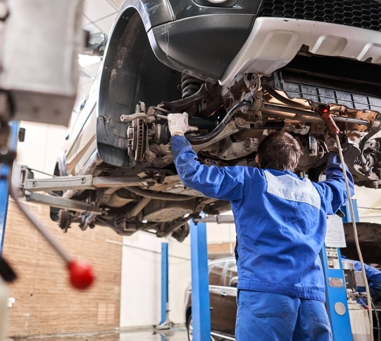 Worker in blue overalls working on an automobile.
